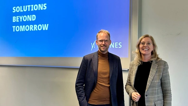 A man and a woman stand in front of a presentation with the words “Solutions beyond tomorrow”.