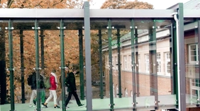 Blick von Außen in den Glasübergang des Campus Neuburg in welchem Studierende gehen.