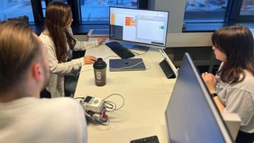 Several students sit around a computer and work together on programming.