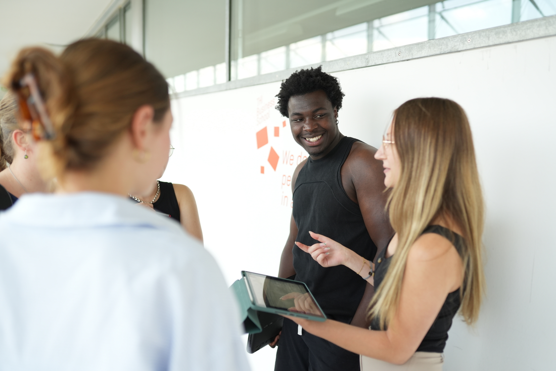 eine Studentin spricht mit 4 weiteren Studierenden. Sie hält ein iPad in ihrer Hand.