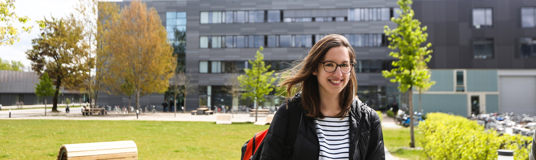 Studentin vor Campuswiese, Gebäude G im Hintergrund