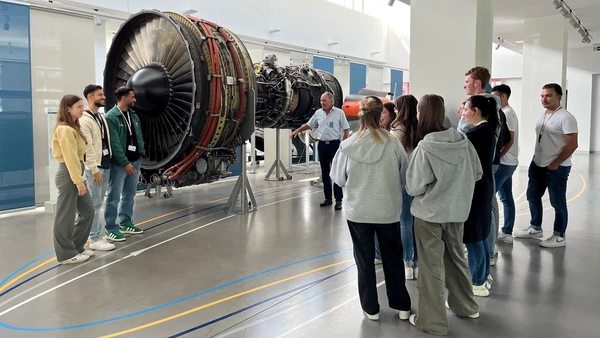 A group of young people and an MTU employee look at a turbine.