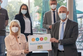 Staatsministerin Carolina Trautner (links) übergibt an Prof. Dr. Schober (rechts) ein Metallschild mit der Aufschrift "Bayern barrierefrei". Im Hintergrund stehen Viktoriya Syedyenkova von der Studierendenvertretung (links) und Staatsminister Bernd Sibler (rechts)