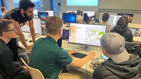 Several students sit around a computer and work together on programming.