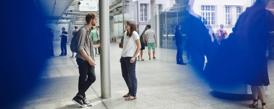 Ein Student und eine Studentin unterhalten sich inmitten anderer Studenten in der Eingangshalle der THI