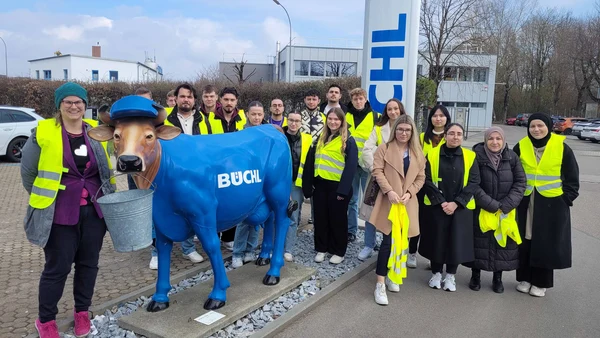 Gruppenphoto auf dem Firmengelände der Firma Büchl, im Vordergrund eine Statue einer blaugefärbten Kuh, die Teilnehmer tragen gelbe Sicherheitswesten