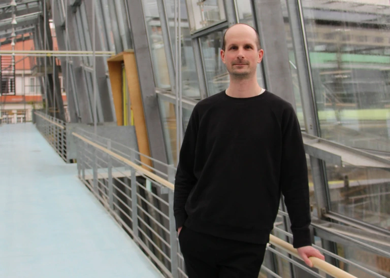 A man dressed in dark clothes in a glass stairwell.