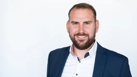 A portrait of a man in his mid-30s with a full beard, dressed in a white shirt and dark jacket.