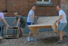 Zwei Männer tragen eine Holzliege, zwei Frauen platzieren einen aus Palettenholz gebauten Tisch