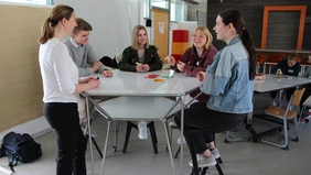 Fünf Personen stehen an einem Tisch und sprechen miteinander.