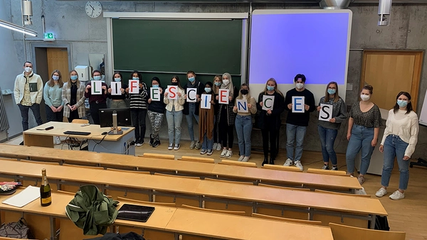 Studierende stehend nebeneinander im Hörsaal und halten Schilder hoch mit dem Schriftzug Life Sciences 