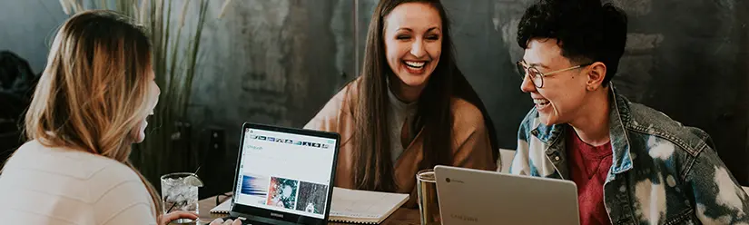 Drei Studenten sitzen in einem Café vor ihren Laptops und lachen