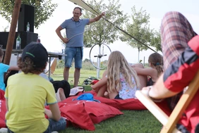 Kinder auf Wiese hören einer Person zu