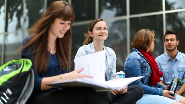 Studierende der Fakultät sitzen vor der Tür auf den Steinen